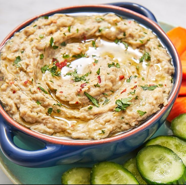 a bowl of dip surrounded by sliced cucumbers and carrots