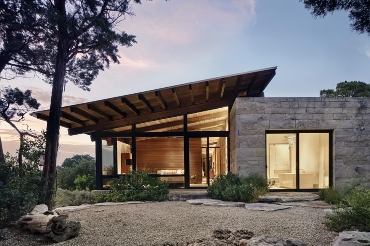 a modern house in the woods with stone walls and roof, surrounded by greenery