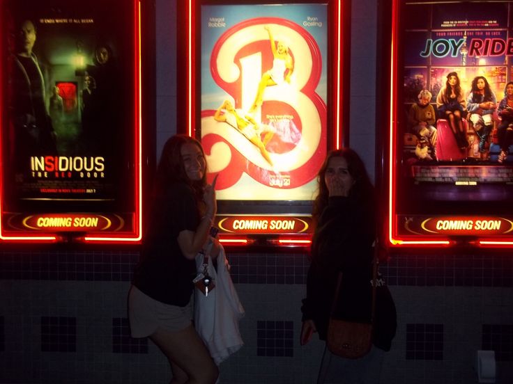 two women standing next to each other in front of some movie posters on the wall