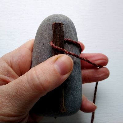 a hand is holding a rock with a cross on it and string attached to it