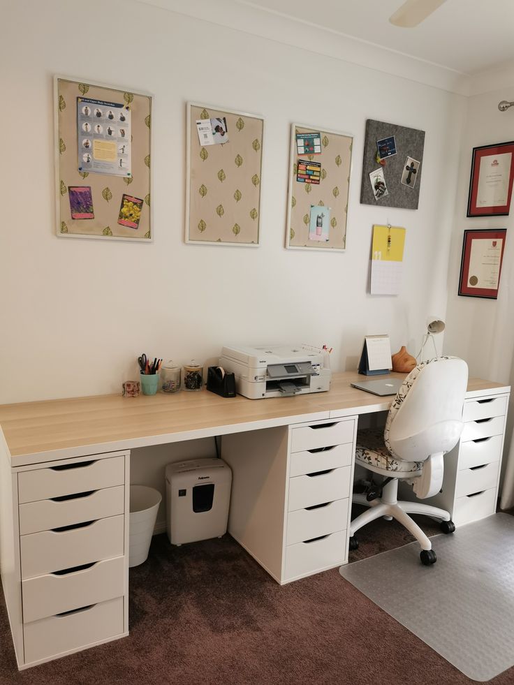 an office desk with drawers, printer and other items on the wall behind it in front of a window