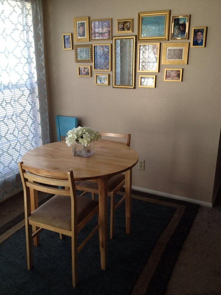 a dining room table with four chairs and pictures on the wall above it, in front of a window