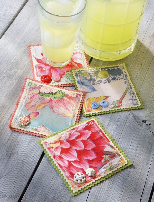 four square coasters with flowers on them next to a glass of lemonade and a drink