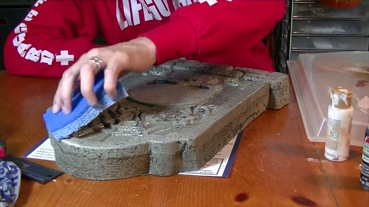 a woman in a red shirt is using a sponge to clean the base of a statue