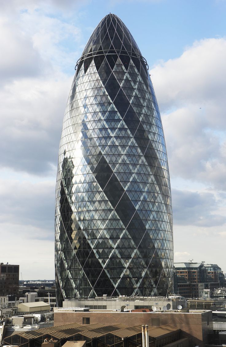 a very tall glass building in the middle of a city with lots of buildings around it