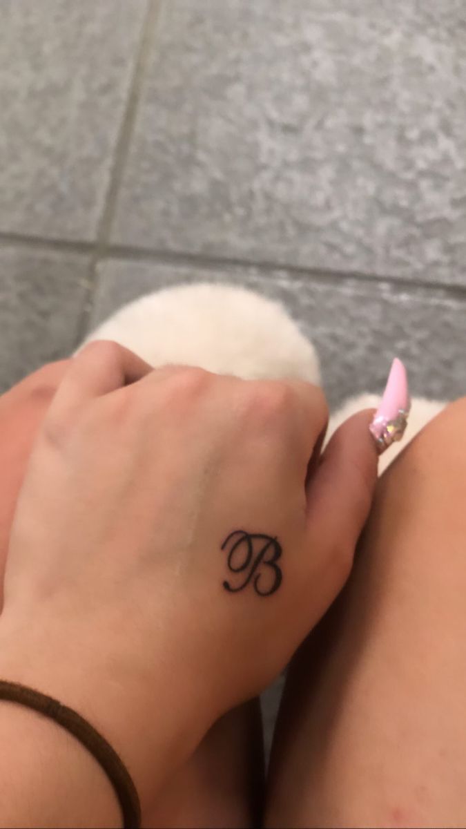 a woman's hand with a small tattoo on her left wrist and the letter b in cursive writing