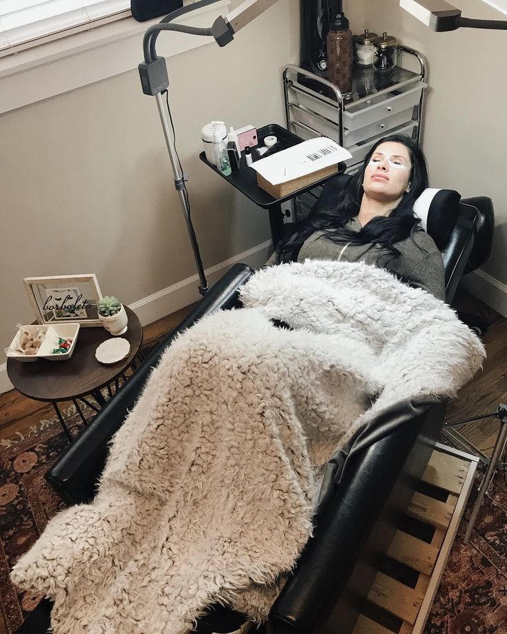 a woman laying on top of a black chair in a living room next to a lamp