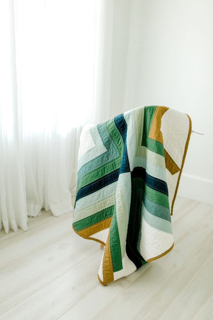 a green and white quilt sitting on top of a wooden floor next to a window