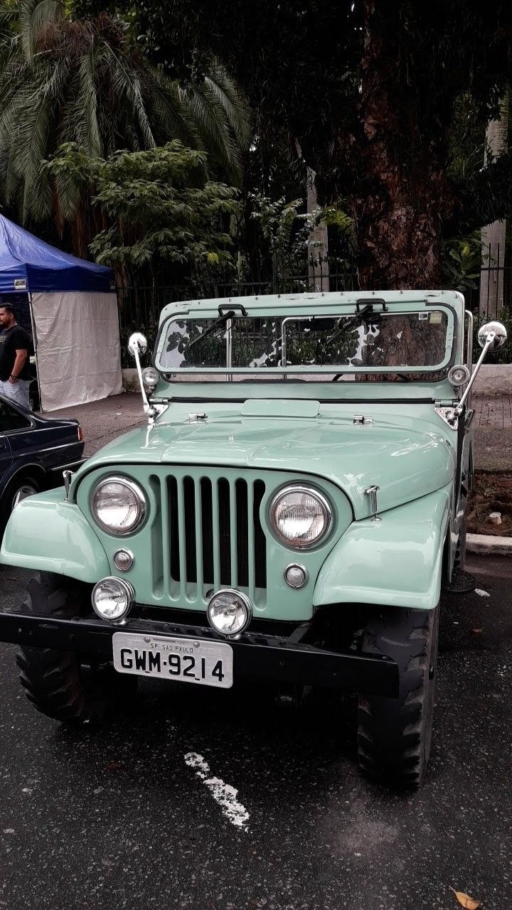 an old green jeep is parked on the street