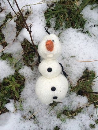 two knitted snowmen sitting on top of grass and snow covered ground in the snow