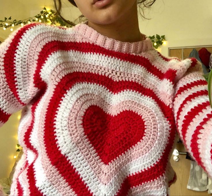 a woman wearing a red and white crocheted sweater with a heart on it