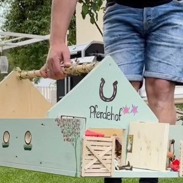 a man is holding a model house made out of wooden pallets and plywood