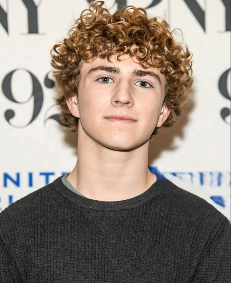 a young man with curly hair standing in front of a wall