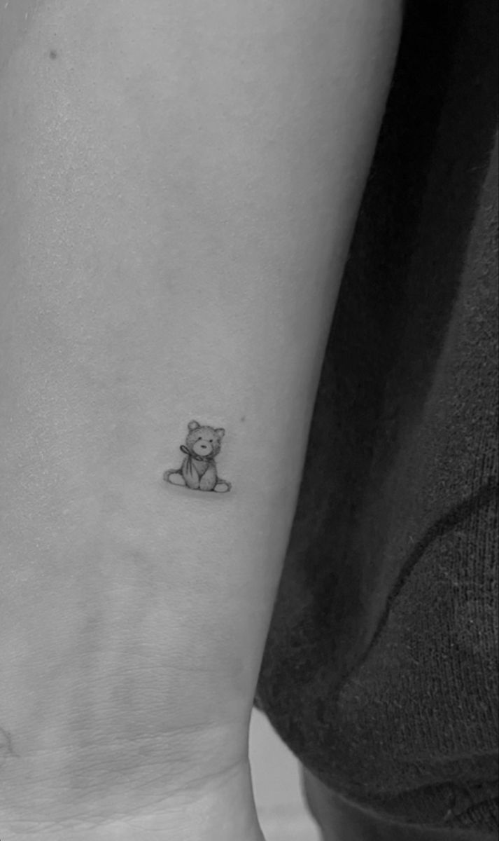 a small teddy bear tattoo on the left inner arm and wrist area is shown in black and white