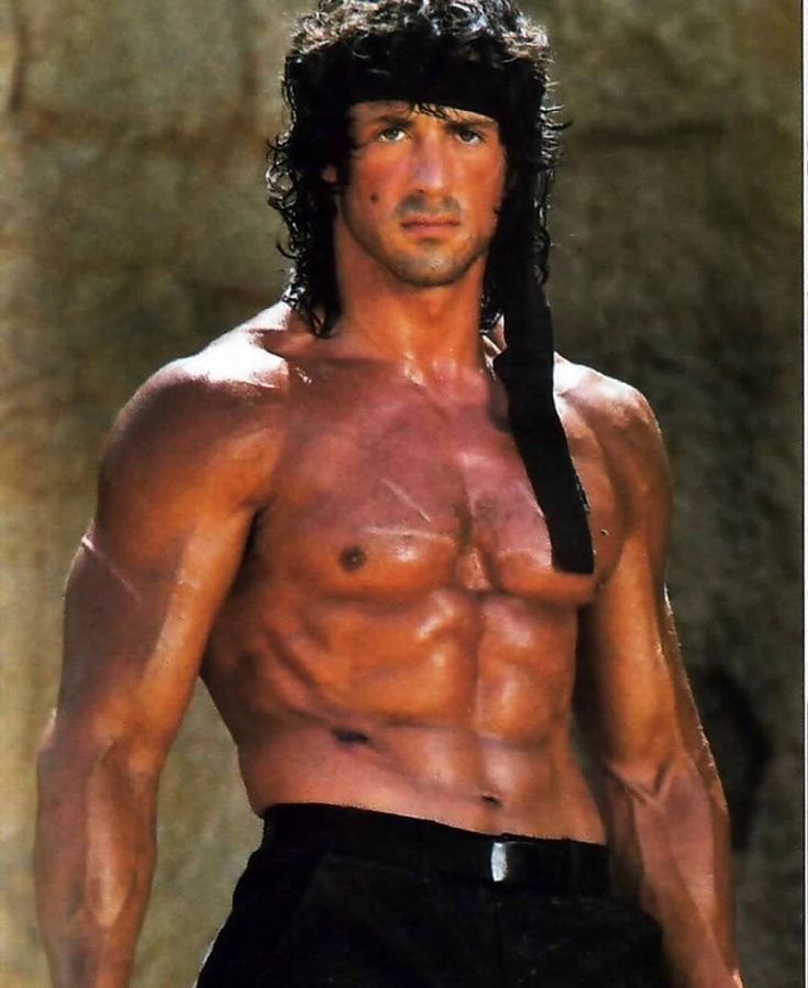 a shirtless man with no shirt on standing in front of a rock face and black hair