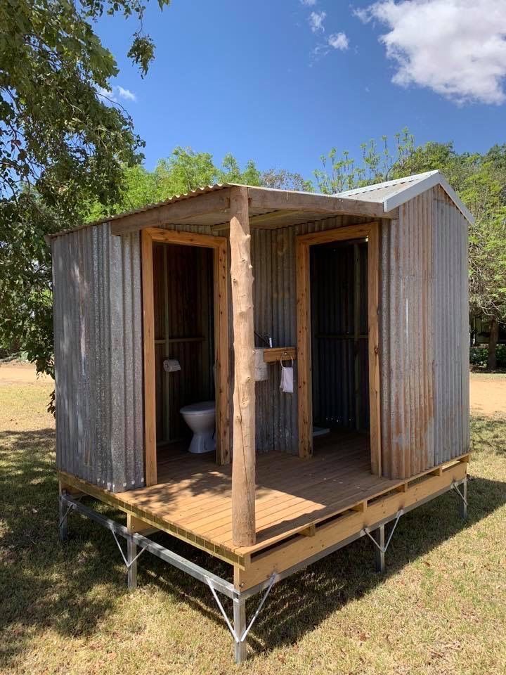 an outhouse with two toilets in it on the side of a grassy field under a blue sky