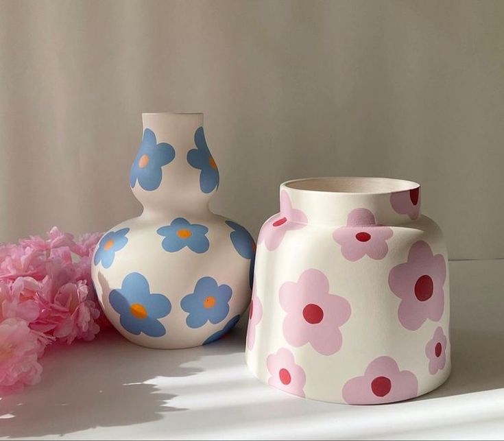 three vases sitting next to each other with pink flowers in front of them on a table