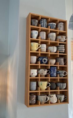 a wooden shelf filled with cups and saucers on top of a white wall next to a window