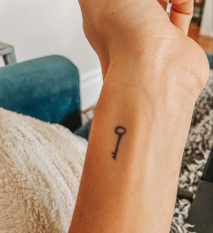 a woman's arm with a small key tattoo on the left side of her wrist