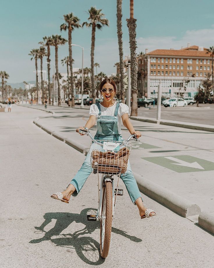 a woman is riding her bike down the street with palm trees in the back ground