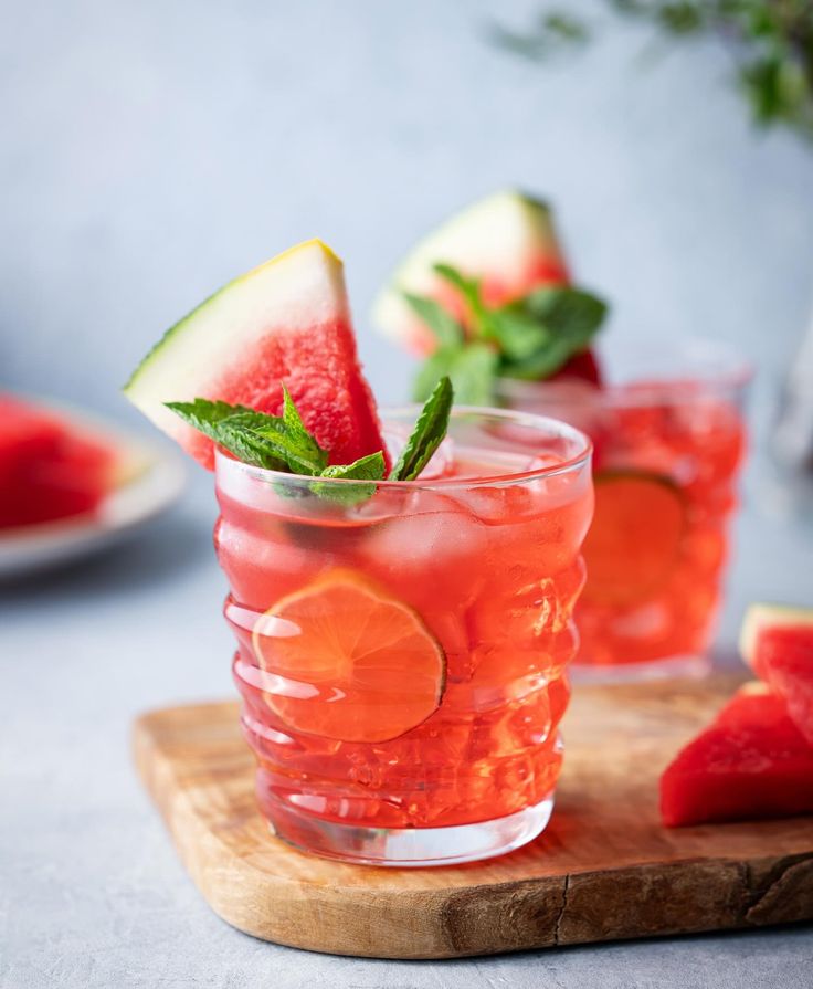 two glasses filled with watermelon and mint garnish on top of a cutting board