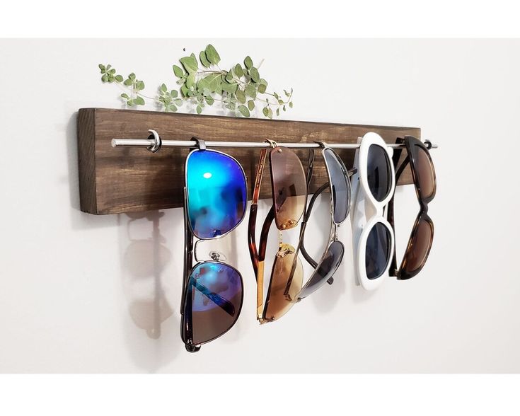 several pairs of sunglasses are hanging on a wooden wall mounted eyeglass holder that holds six pairs of sunglasses