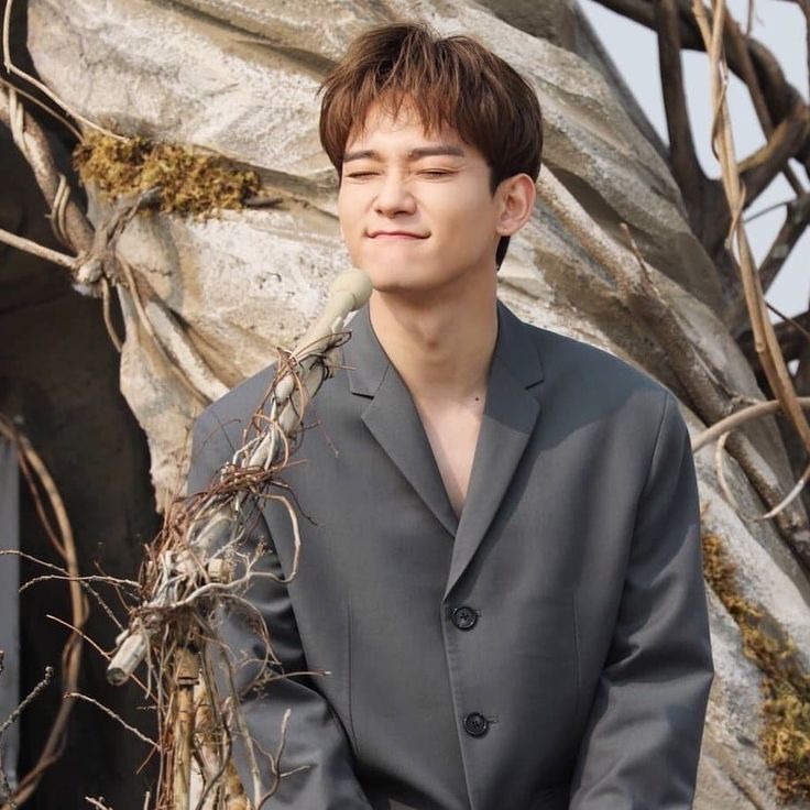 a young man wearing a suit and tie standing in front of a rock formation with dry grass growing on it