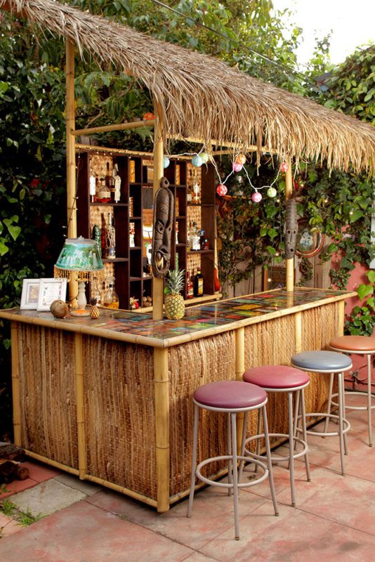 a tiki bar with stools in front of it and plants around the bar