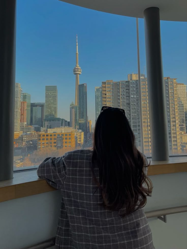 a woman looks out the window at the city skyline in toronto, on a sunny day