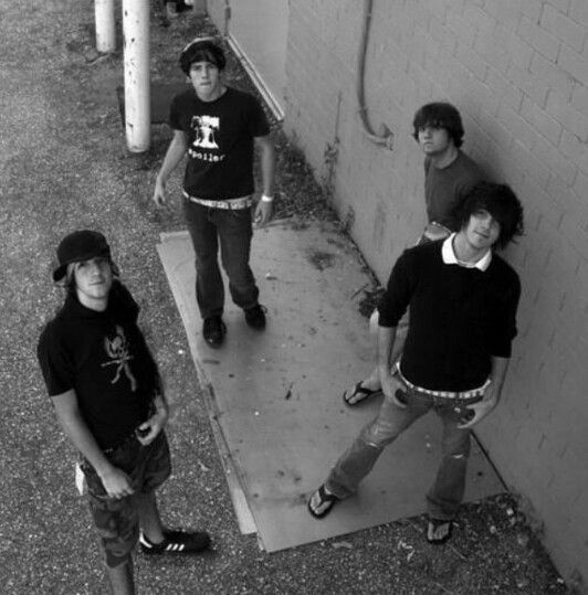 four young men standing in front of a building with no one around them looking at the camera