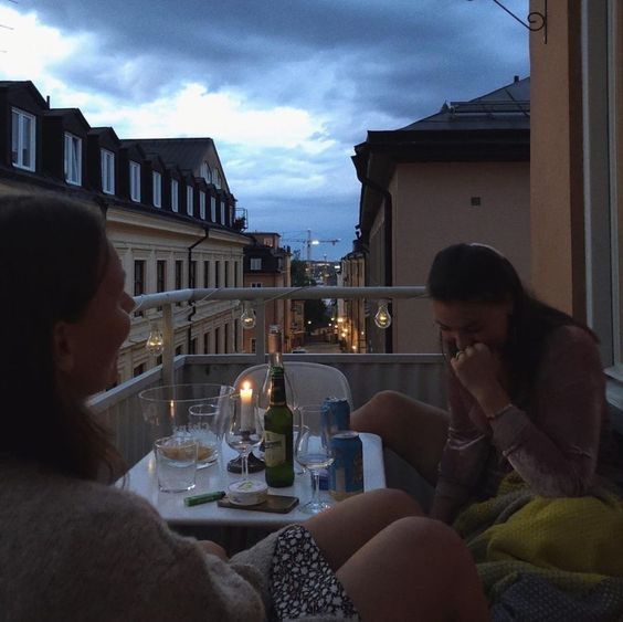 two women sitting at a table on a balcony with bottles and glasses in front of them