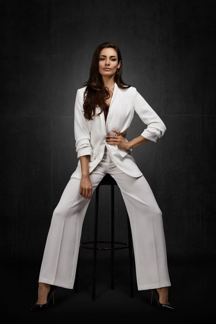 a woman sitting on top of a stool wearing white pants and a blazer jacket