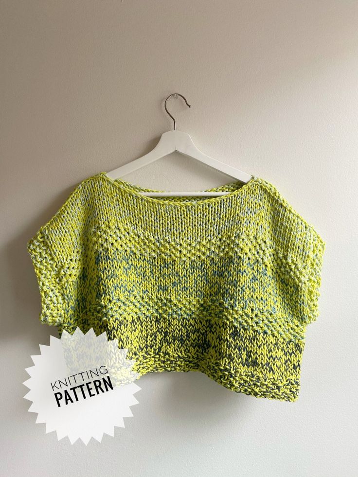 a green knitted sweater hanging on a white wall with a badge stating knitting pattern