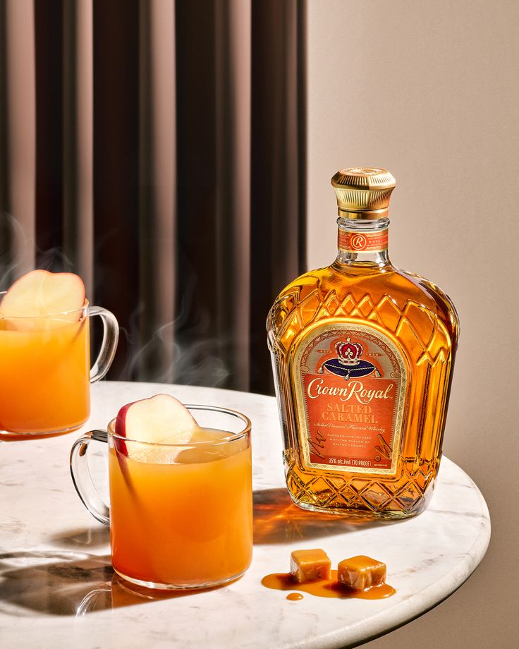 a bottle of crown royal whisky next to two glasses filled with orange juice and ice cubes