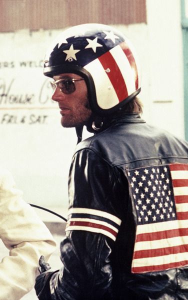 two men in leather jackets and american flags on the back of their motorcycles, one wearing a motorcycle helmet