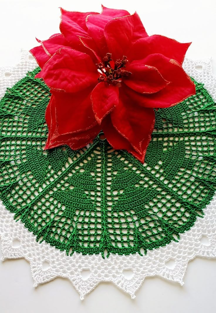 a red poinsettia sitting on top of a doily with green trim