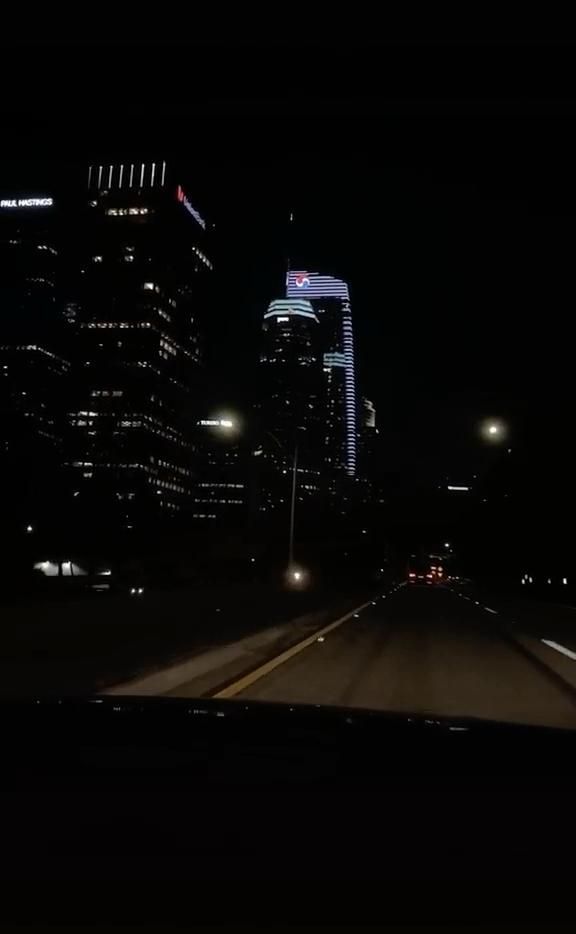 the city skyline is lit up at night with street lights and skyscrapers in the background