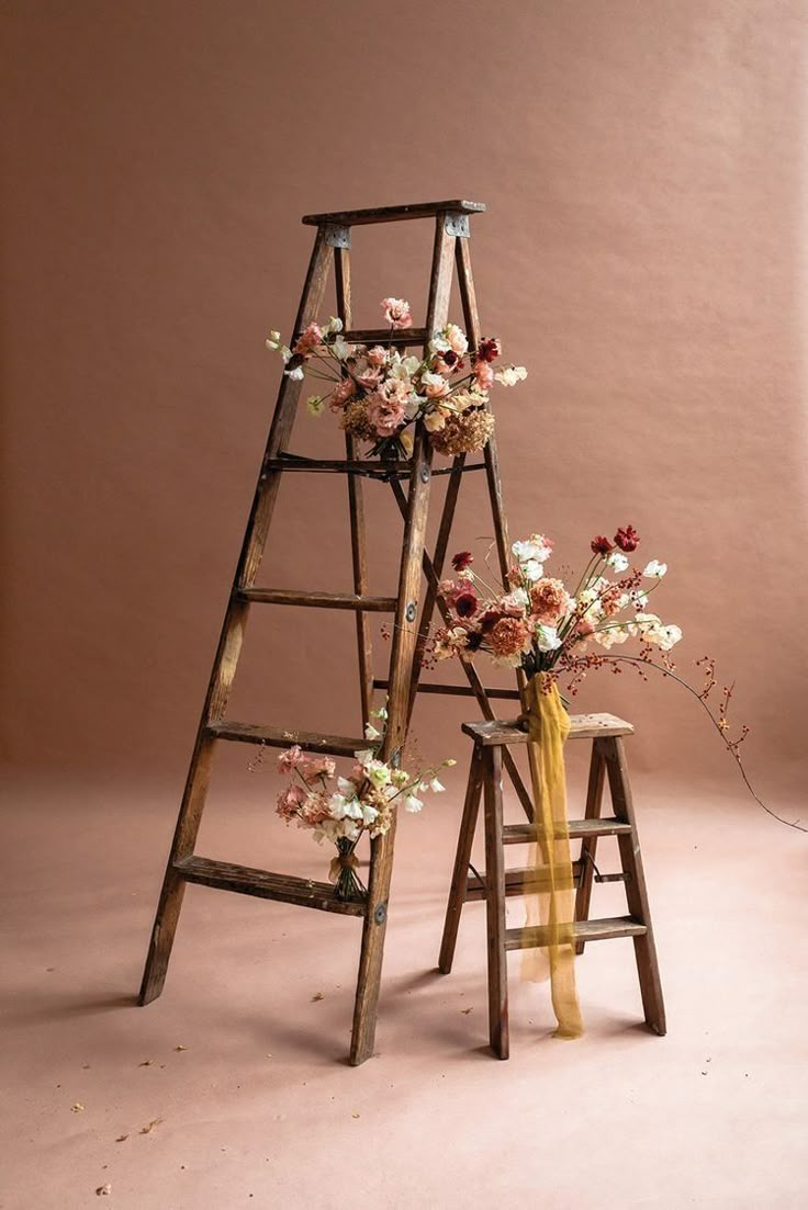 an old ladder with flowers on it next to a small wooden stool and vase filled with flowers