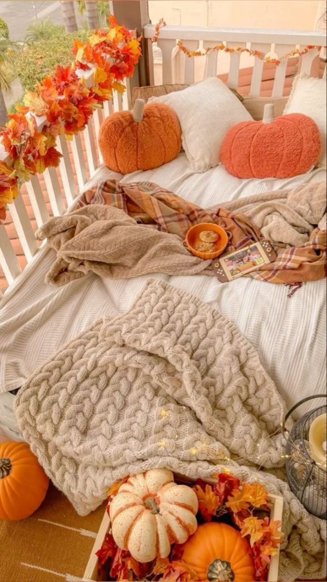 a bed covered in blankets and pumpkins on top of a wooden floor next to flowers