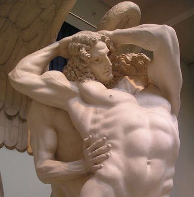 a statue of two men hugging each other in front of a wall with angel wings