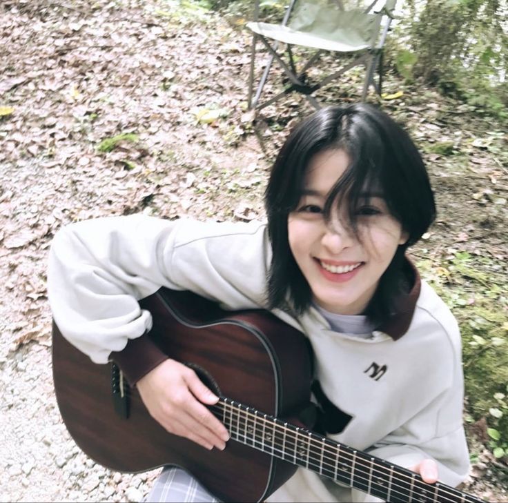 a woman sitting on the ground with an acoustic guitar in her hand and smiling at the camera