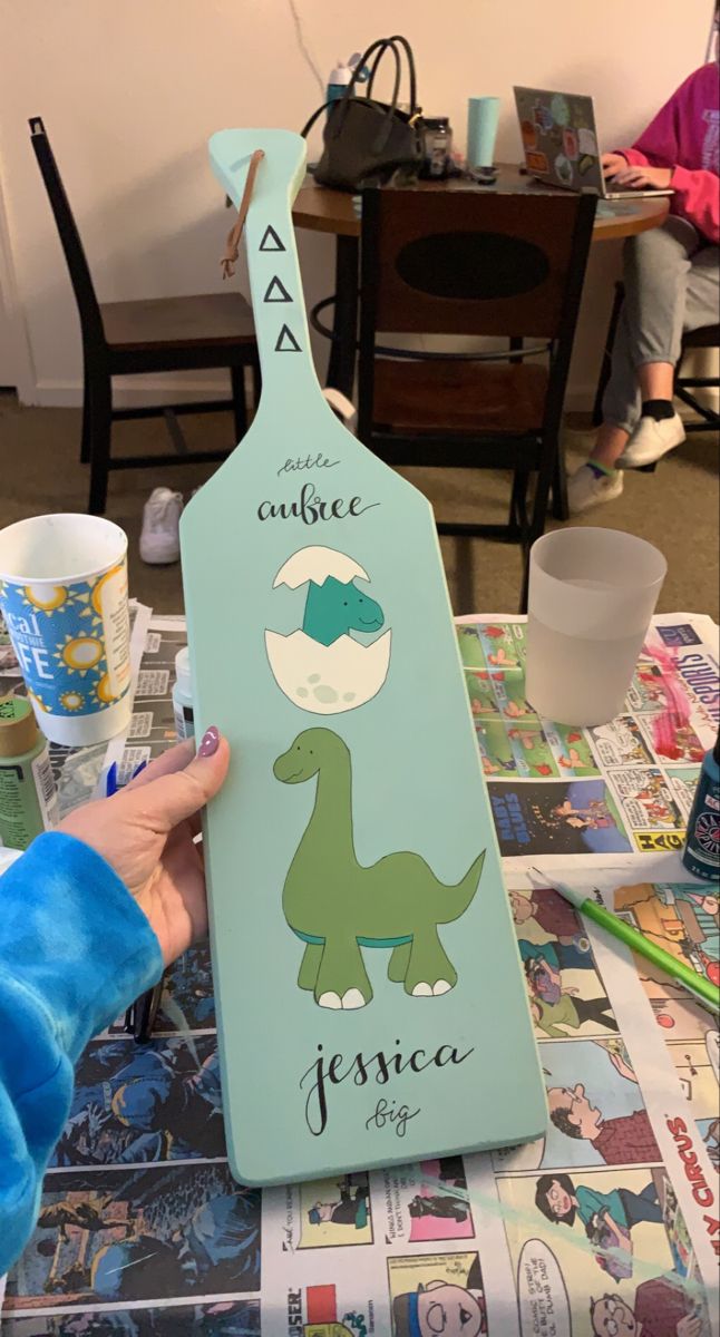 a child's hand is holding up a wooden sign with the name and image of a dinosaur on it