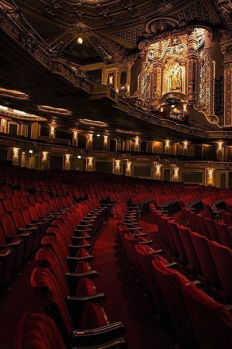 an empty theater with red seats and chandeliers on the ceiling is lit up