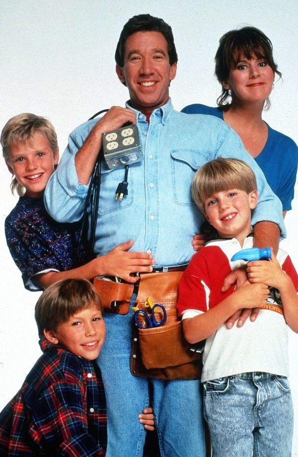 the family is posing for a photo with their cell phone in hand and one man holding two children