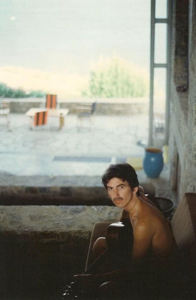 a shirtless man sitting on the ground in front of an open window looking at something