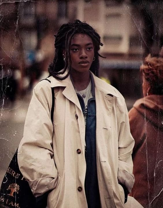 a woman with dreadlocks is walking down the street while wearing a trench coat