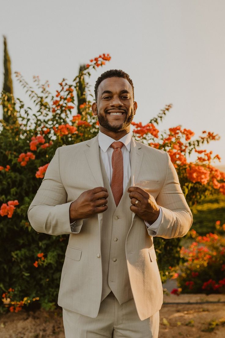 a man in a suit and tie is smiling at the camera with flowers behind him