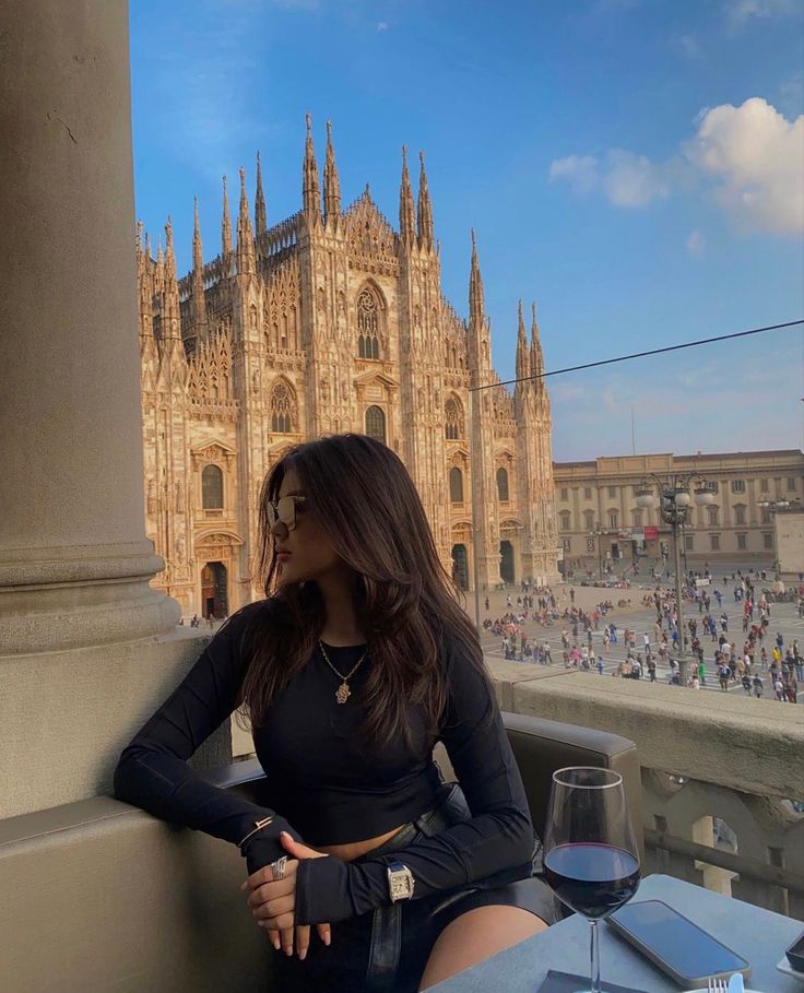 a woman is sitting on a balcony with a glass of wine in front of her