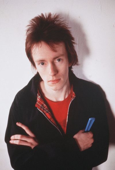 a young man with his arms crossed standing in front of a white wall