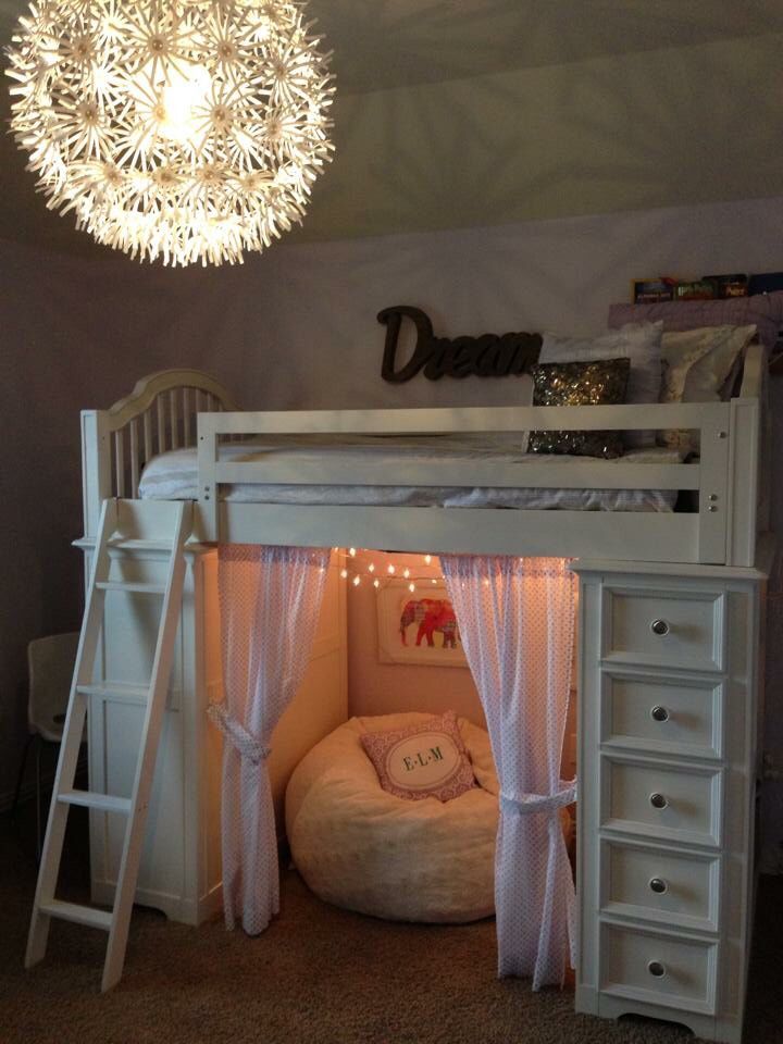 a white bunk bed sitting under a light next to a desk with drawers underneath it